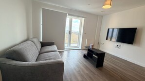 A modern living room with a grey sofa, a black TV stand, and a large flat-screen TV.