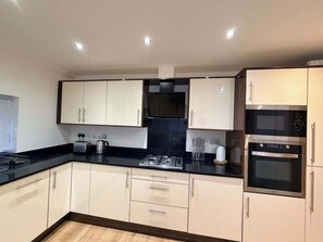 A modern kitchen with white cabinets, black countertops, and stainless steel appliances including a stove, microwave, and oven. - Sleek Modern 2BDR Flat in Charming Pinner (Greater London)