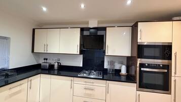 A modern kitchen with white cabinets, a black countertop, and stainless steel appliances including a stove, oven, and microwave.