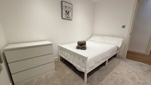 A bedroom with a bed, a white dresser, a rolled towel on the bed, and a framed picture on the wall.