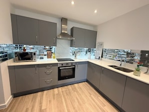 A modern kitchen with grey cabinets, a stainless steel range hood, a built-in oven, and a double sink. - Sleek Modern 2BDR Flat in Charming Pinner (Greater London)