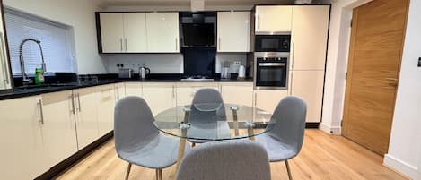 Une cuisine moderne avec une table à manger en verre et des chaises grises, un plancher en bois et des appareils électroménagers intégrés.