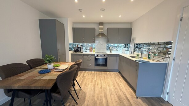 A modern kitchen with grey cabinets, a wooden dining table, and a built-in oven.