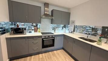 A modern kitchen with grey cabinets, a stainless steel range hood, a built-in oven, and a double sink.