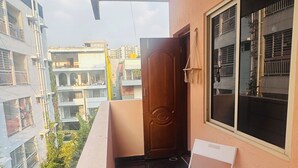 Ein Balkon mit zwei weißen Klappstühlen, einer Holztür und einem Fenster mit Rollläden.