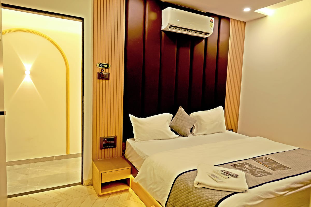 Une chambre d’hôtel avec un lit, un marchepied intégré, un climatiseur fixé au mur et une porte dotée d’un éclairage.