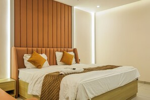 A modern hotel room with a large bed, wooden headboard, and a neutral color scheme. - Hotel VD Rooms Vesu (Surat)