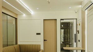 Una habitación de hotel moderna con un sofá seccional color beige, una mesita y una puerta que da a un pasillo.