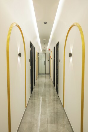 A long, narrow hotel corridor with a shiny tiled floor and walls accented with gold trim. - Hotel VD Rooms Vesu (Surat)