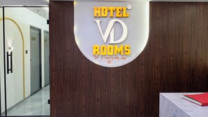 Zona de recepción de un hotel con diseño moderno, que incluye un mostrador de recepción, una araña y un cartel que dice 'HOTEL VRD ROOMS'.