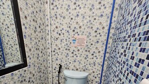 Un baño con inodoro, lavamanos y espejo. Las paredes tienen azulejos con un diseño azul y blanco.
