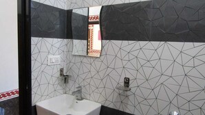 Een badkamer met een wit wastafelmeubel, twee kraanwerkstukken en een spiegel. De muren zijn betegeld met een geometrisch patroon.