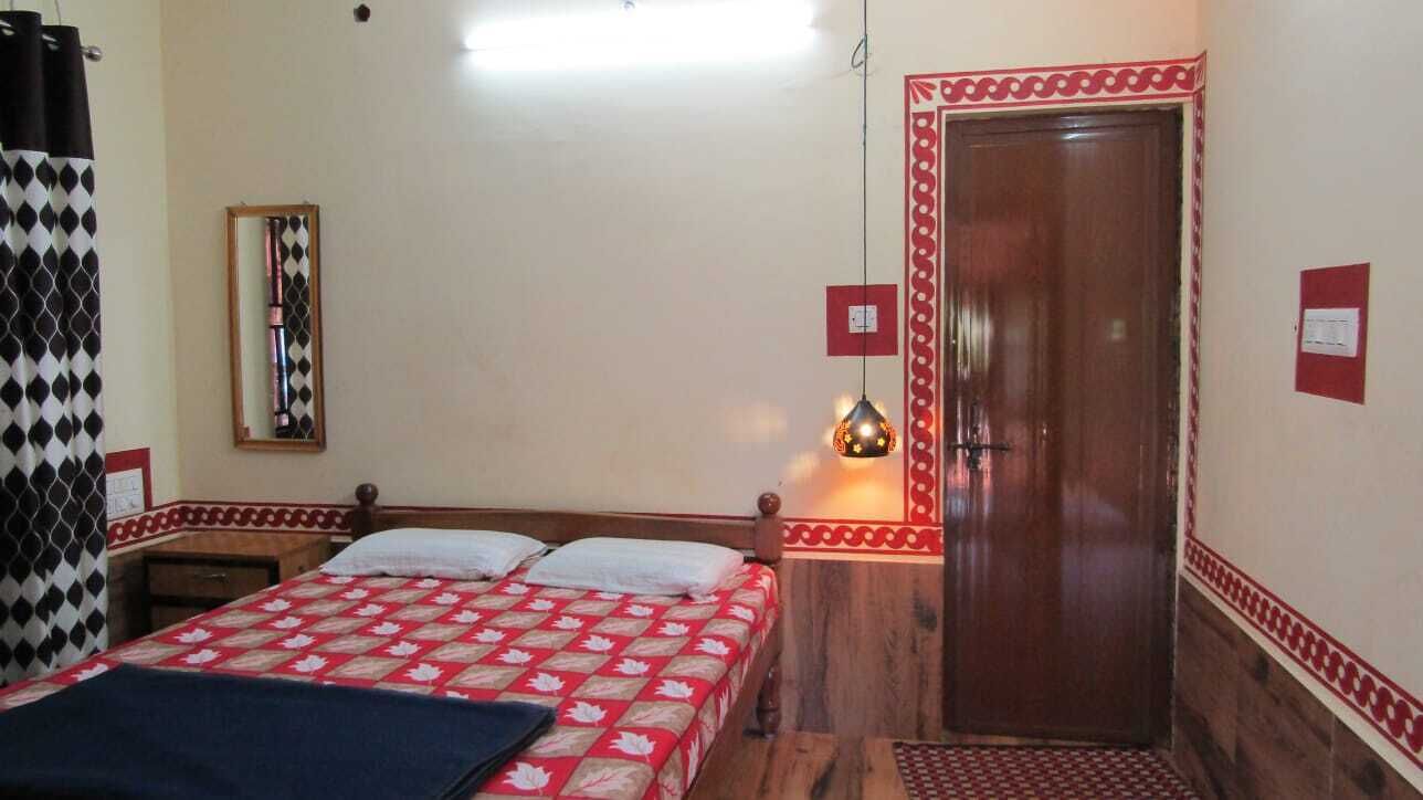A bedroom with a bed, a wooden door, a mirror, and a wall-mounted light fixture.