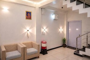A reception area with a sofa, wall-mounted lights, a trash bin, a potted plant, and a staircase. - Hotel Rukhmani Residency (Ujjain)