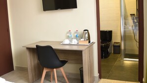 Een hotelkamer met een bed, een bureau met stoel, een televisie, een douche en een toilet.