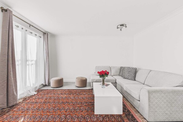 A modern living room with a white sofa, a white coffee table, and a patterned rug.
