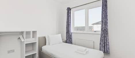 A bedroom with a bed, a wardrobe, and a window with curtains.