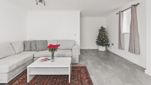Ein modernes Wohnzimmer mit grauem Sofa, weißem Couchtisch, einem gemusterten Teppich und einem Weihnachtsbaum.