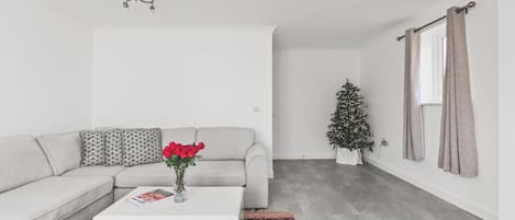 A modern living room with a grey sofa, a white coffee table, a patterned rug, and a Christmas tree.