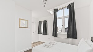 A modern bedroom with a large bed, a window with curtains, a radiator, and a door. - Beautiful 4BDR Townhouse with Free Parking (Hayes)