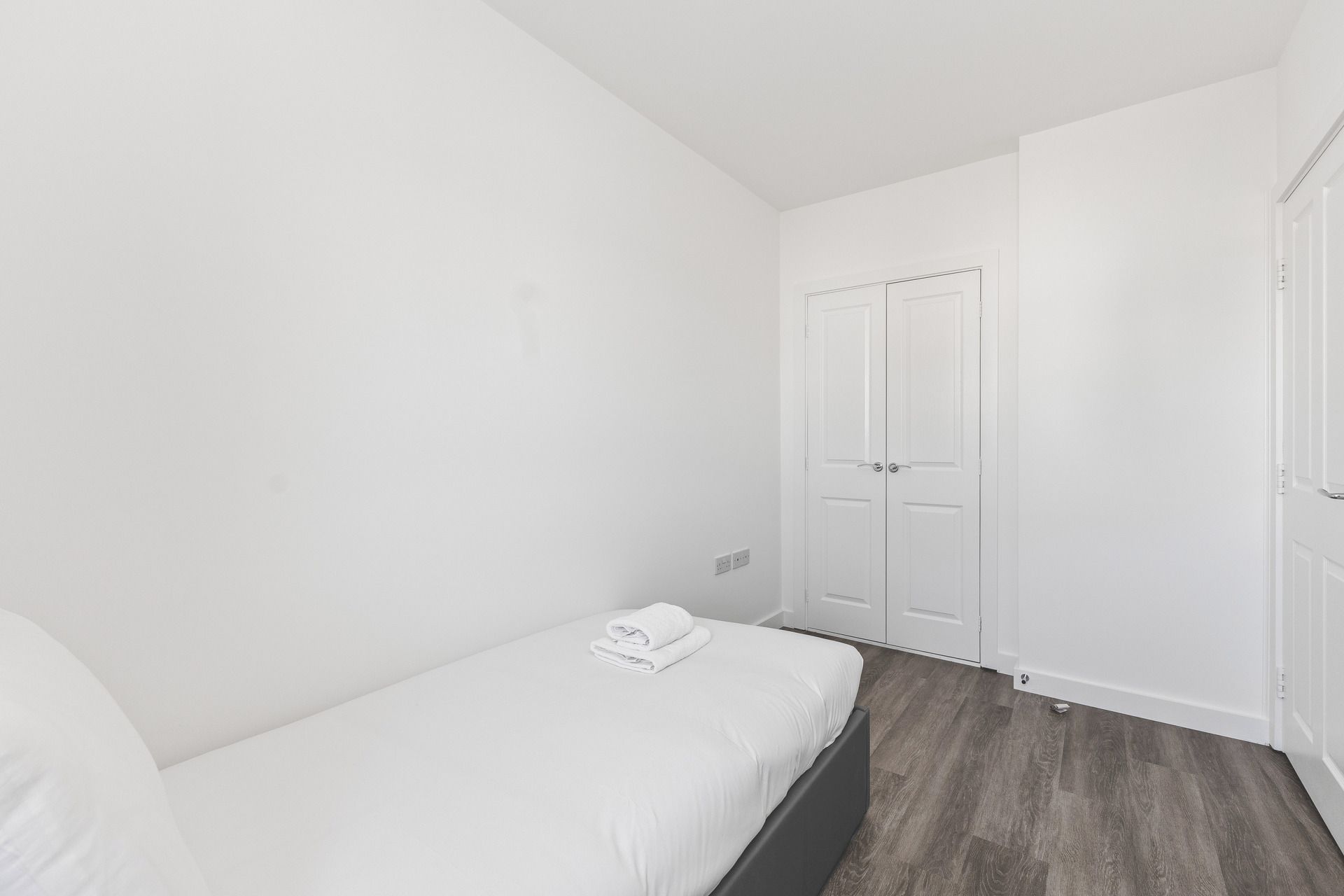 A small, white room with a single bed, a wardrobe, and a door.