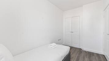 A small, white room with a single bed, a wardrobe, and a door.