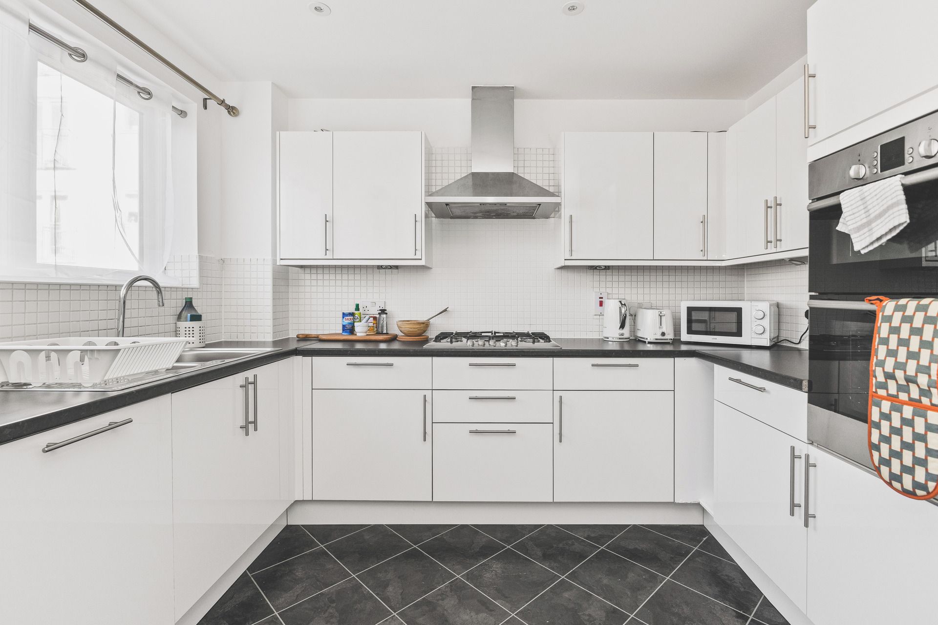 A modern kitchen with white cabinets, a gas stove, a microwave, and a black tiled floor.