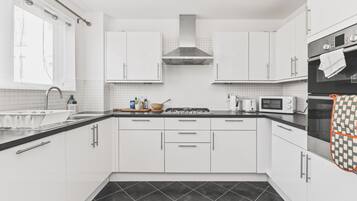A modern kitchen with white cabinets, a gas stove, a microwave, and a black tiled floor.