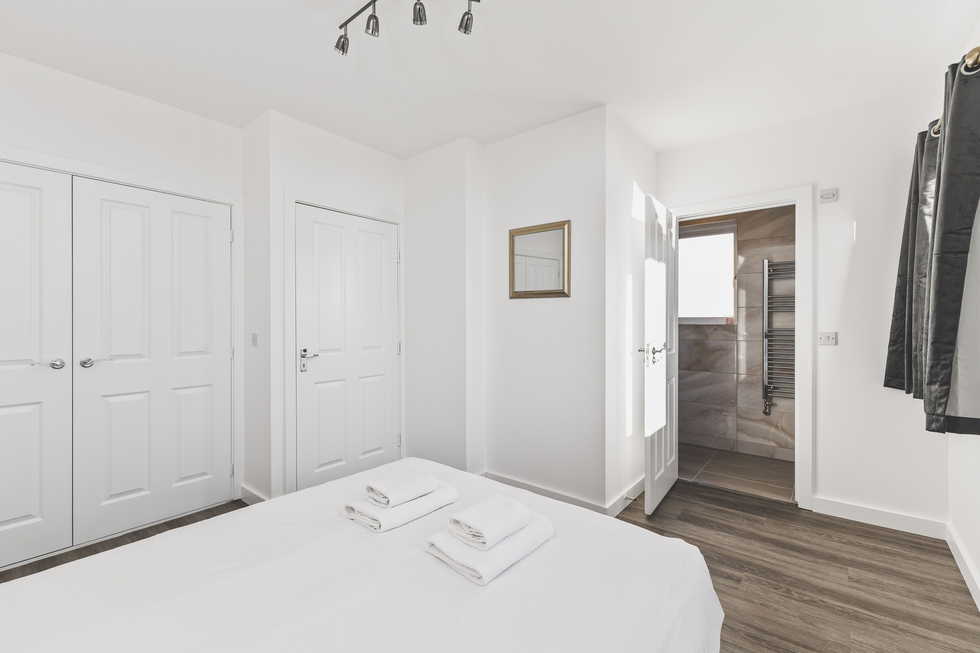 Habitación de hotel con cama, armario, espejo y baño con perchero.