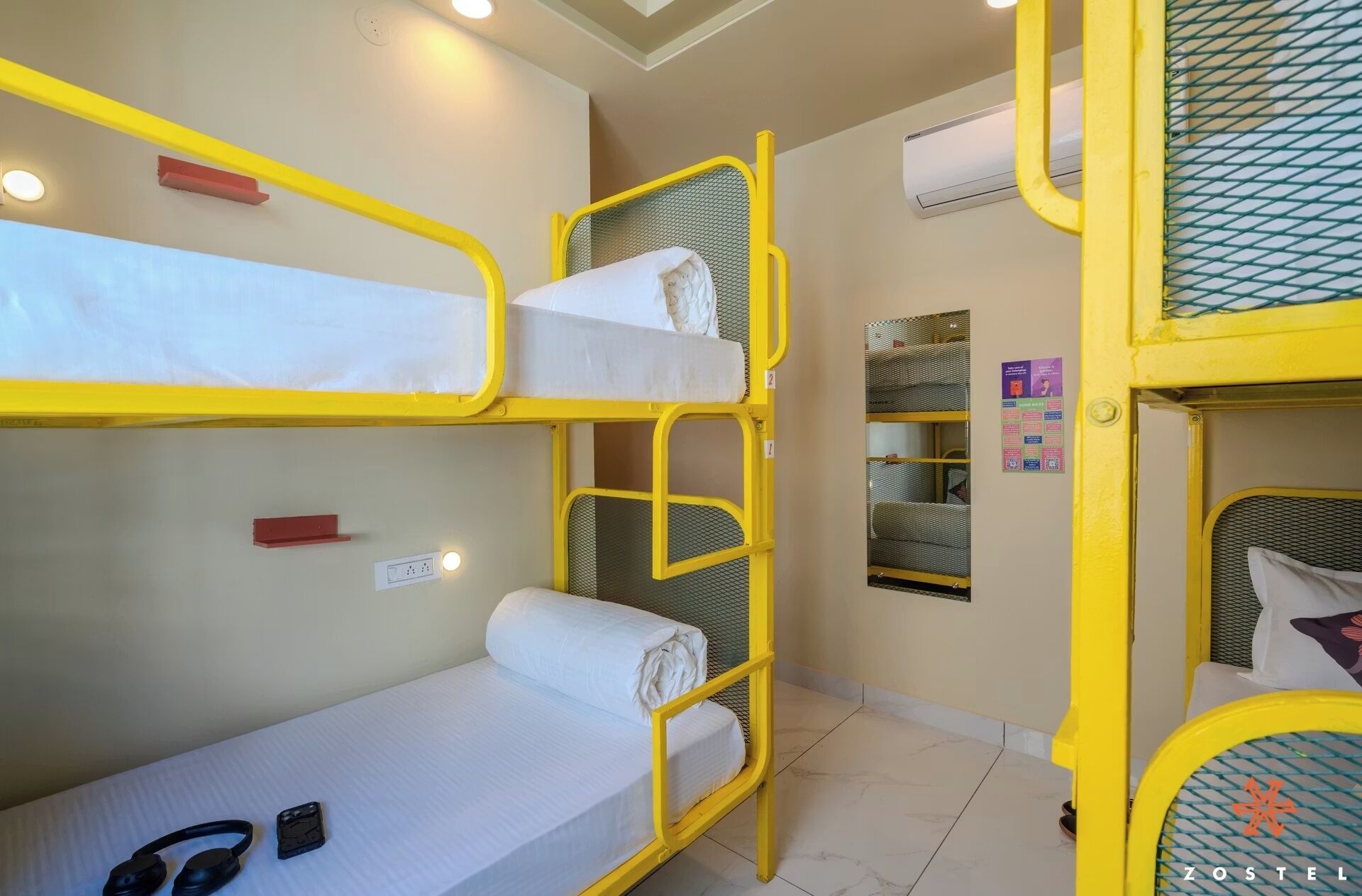 Habitación con literas de estructura amarilla, colchón blanco y un par de auriculares en el suelo.
