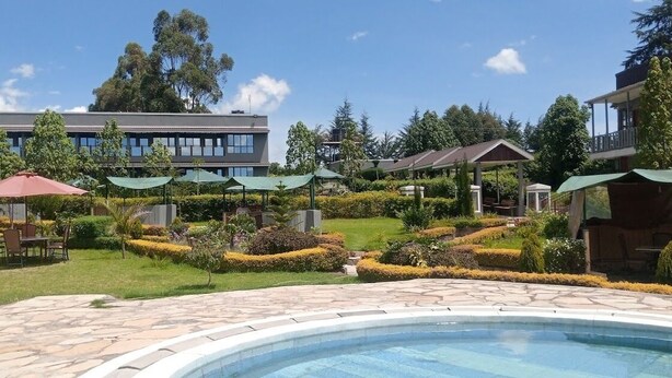 A pool area with a stone deck, surrounded by well-manicured gardens and outdoor seating. - Olempiaus Gardens Hotel (Engineer)