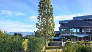 A modern building with a flat roof and large windows, surrounded by landscaped gardens with various plants and a stone pathway. - Olempiaus Gardens Hotel (Engineer)