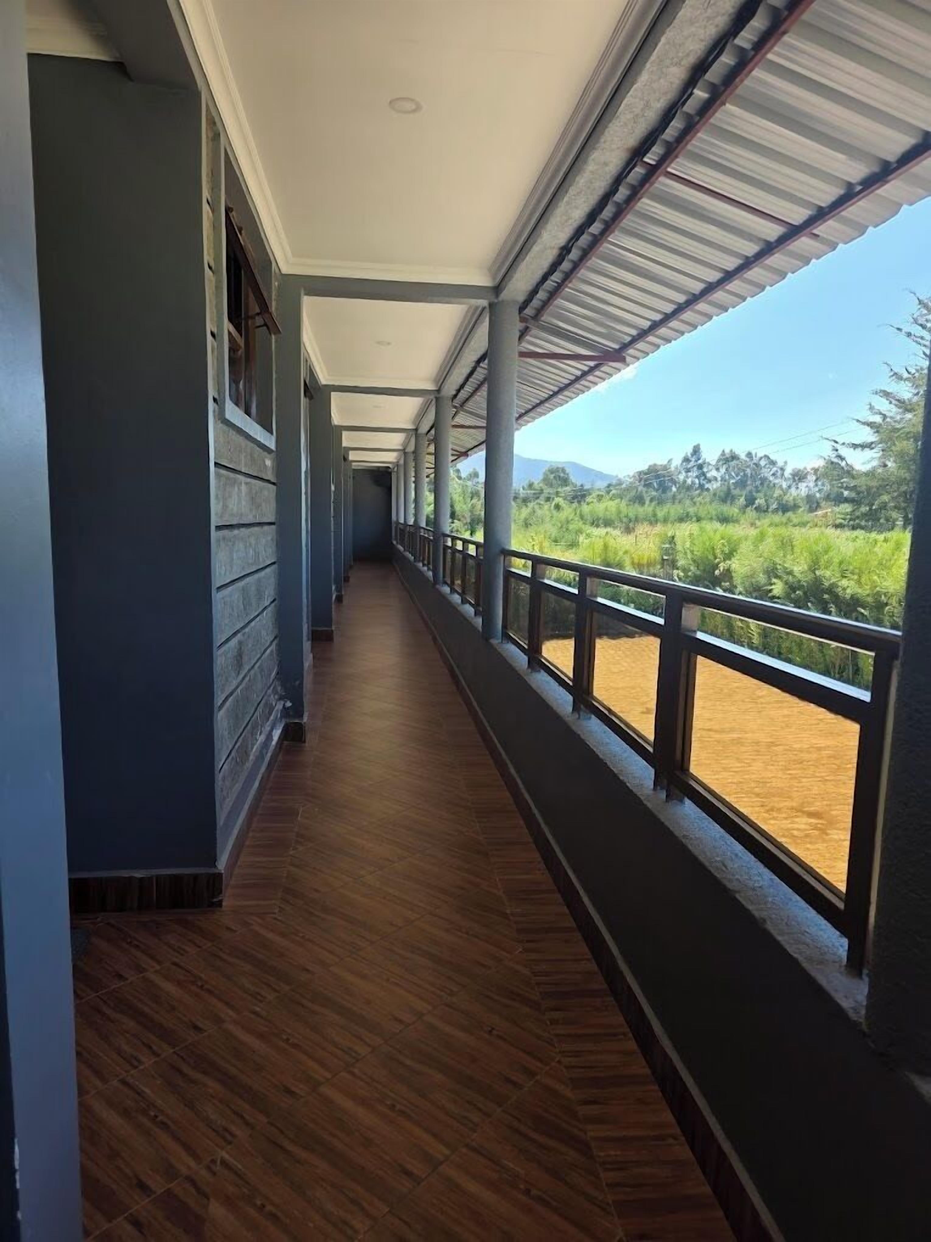 A covered corridor with wooden flooring and large windows offering a view of a river and greenery.