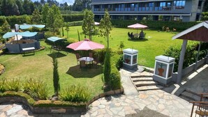 A courtyard with outdoor seating, stone pathways, and a building in the background. - Olempiaus Gardens Hotel (Engineer)