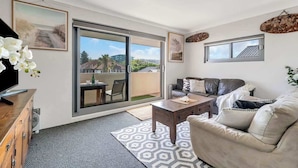 A modern living room with a large sliding glass door leading to a balcony, a sofa, a coffee table, and a TV on a wooden cabinet. - Bondi Beach Breeze - Walk to Beach and Shops (Bondi Beach)