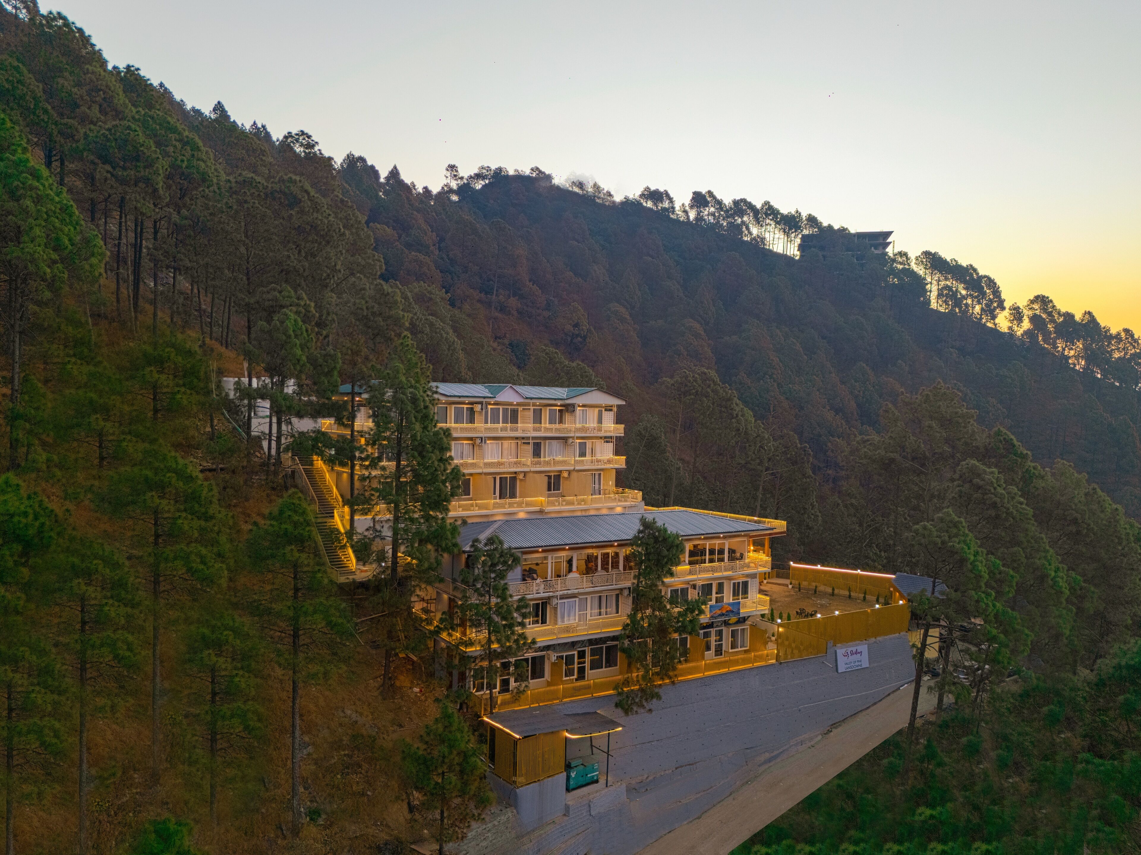 A multi-story hotel with a balcony on the second floor, surrounded by forested hills.