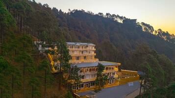 A multi-story hotel with a balcony on the second floor, surrounded by forested hills.