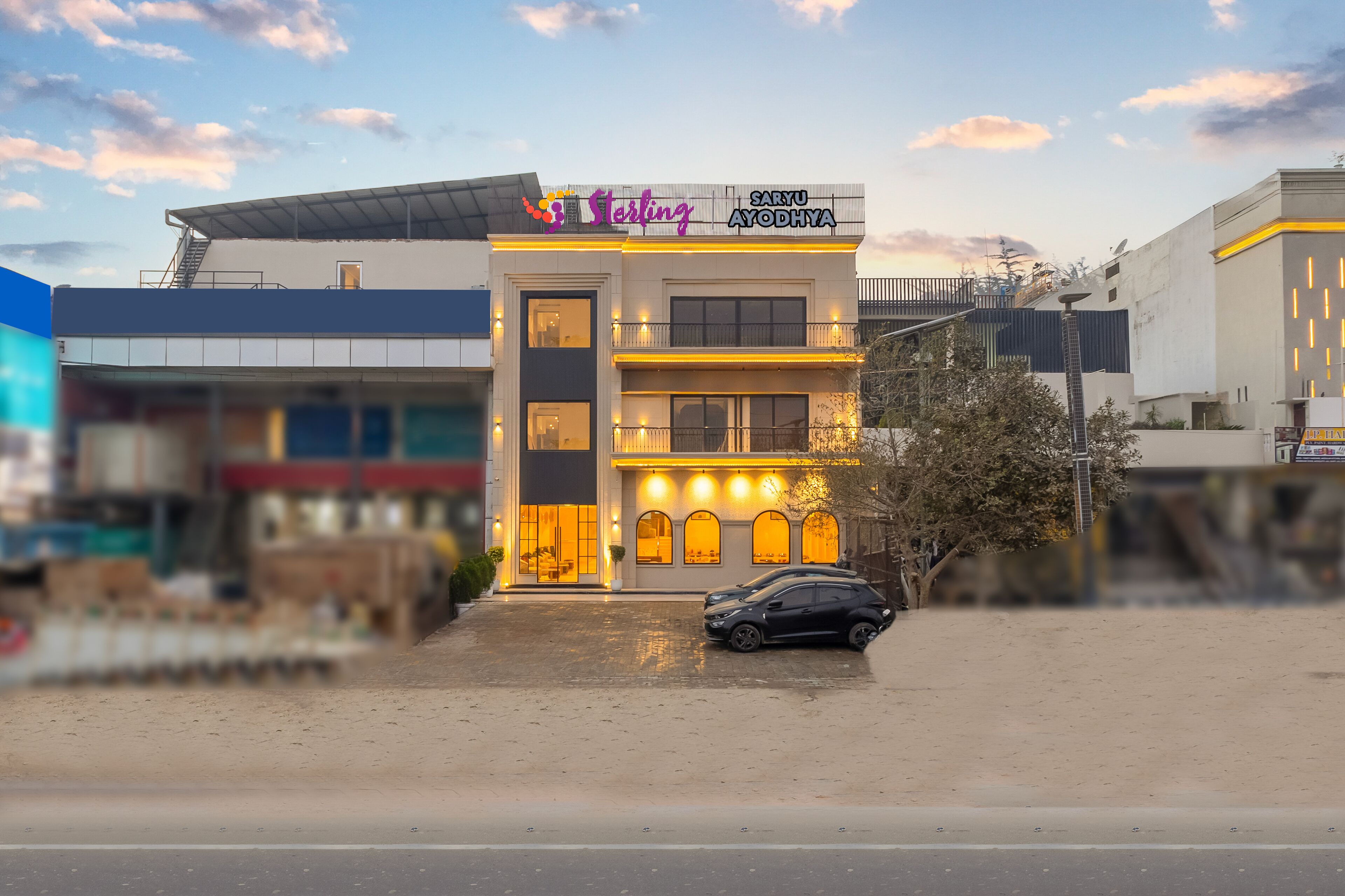 Un edificio moderno con un letrero que dice "Saru Ayodhya" y "Starling". Tiene techo plano, una escalera y un coche estacionado en frente.
