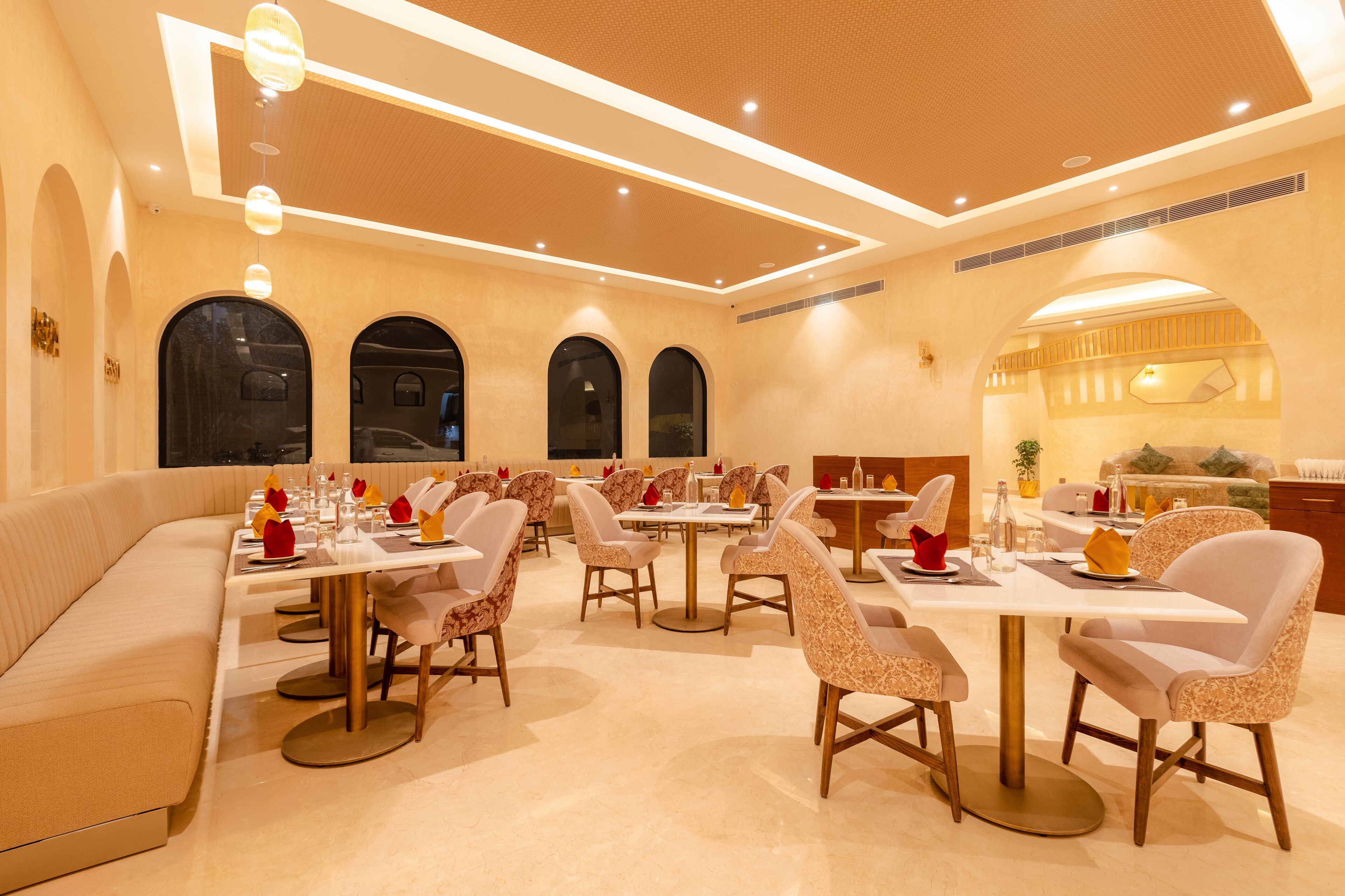 Uma sala de jantar ampla, com várias mesas e cadeiras, destacando uma paleta de cores quentes e iluminação moderna.