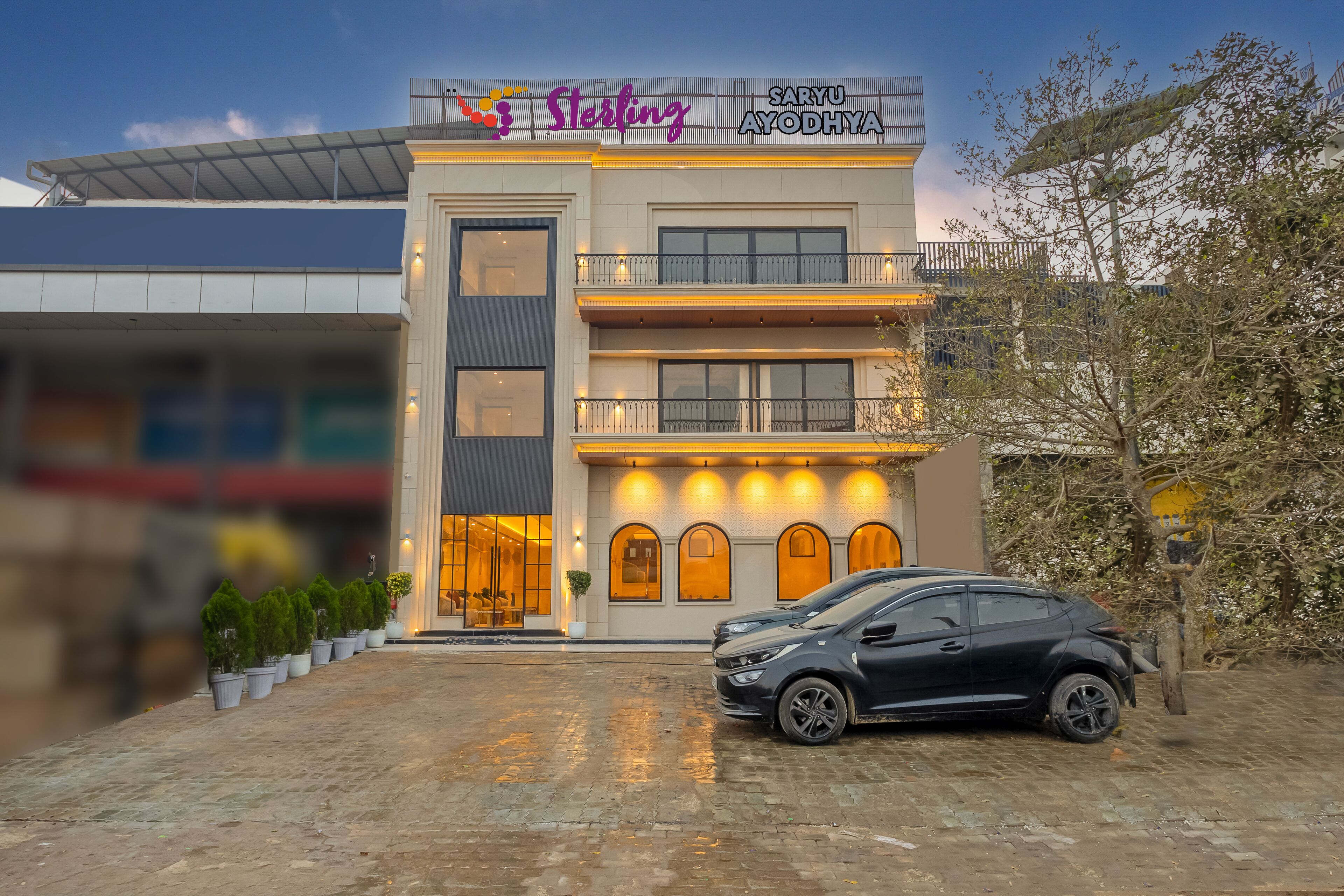 A building with a sign reading "Sterling Saryu Ayodhya" and a black car parked in front.