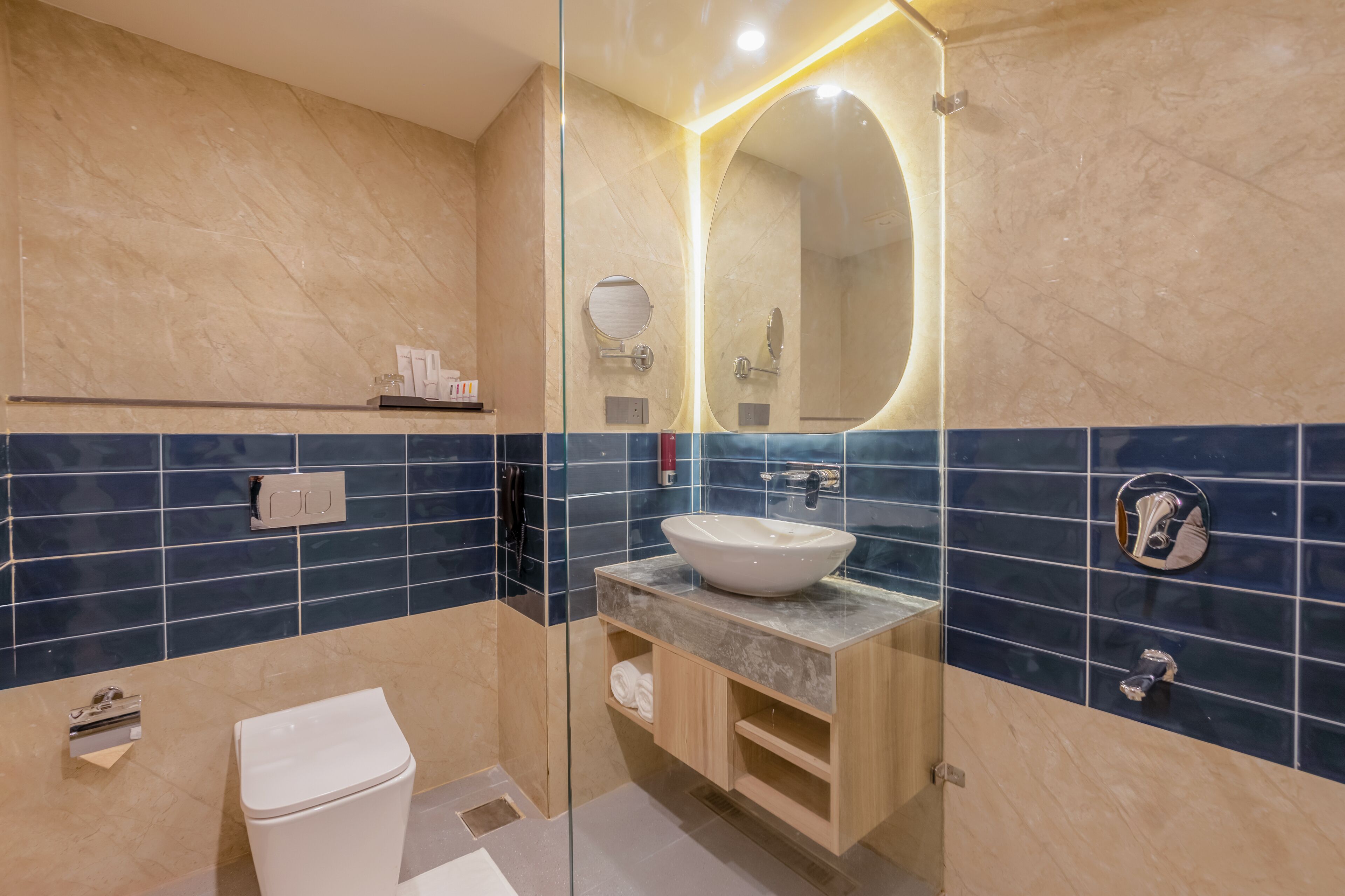 A modern bathroom with a glass partition, a white toilet, a sink with a marble countertop, and a mirror with a circular frame.