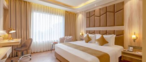 A hotel room with a large bed, a desk, a chair, and a sofa.