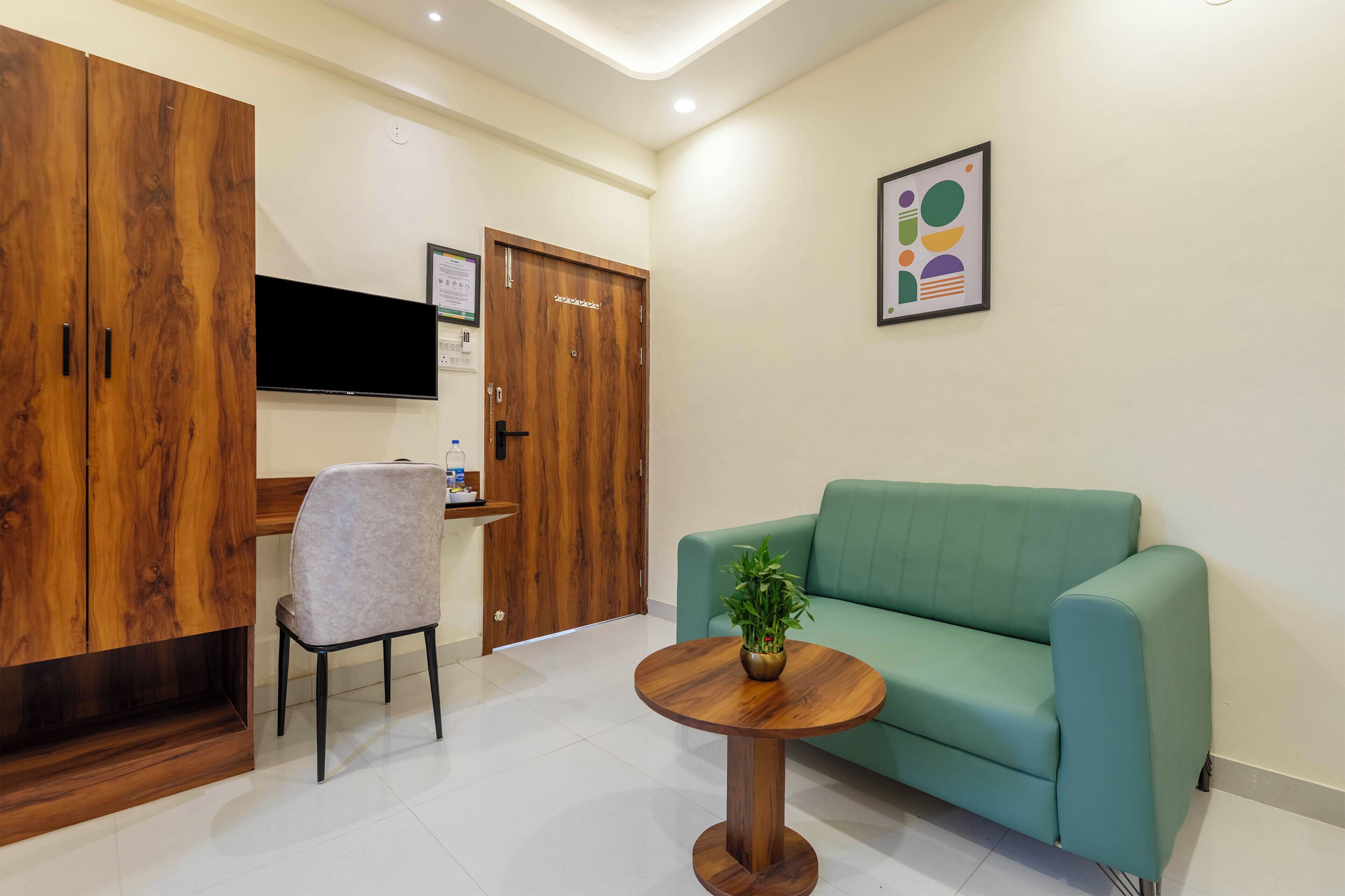 A room with a green sofa, a wooden cabinet, a TV mounted on the wall, and a small round table with a plant.