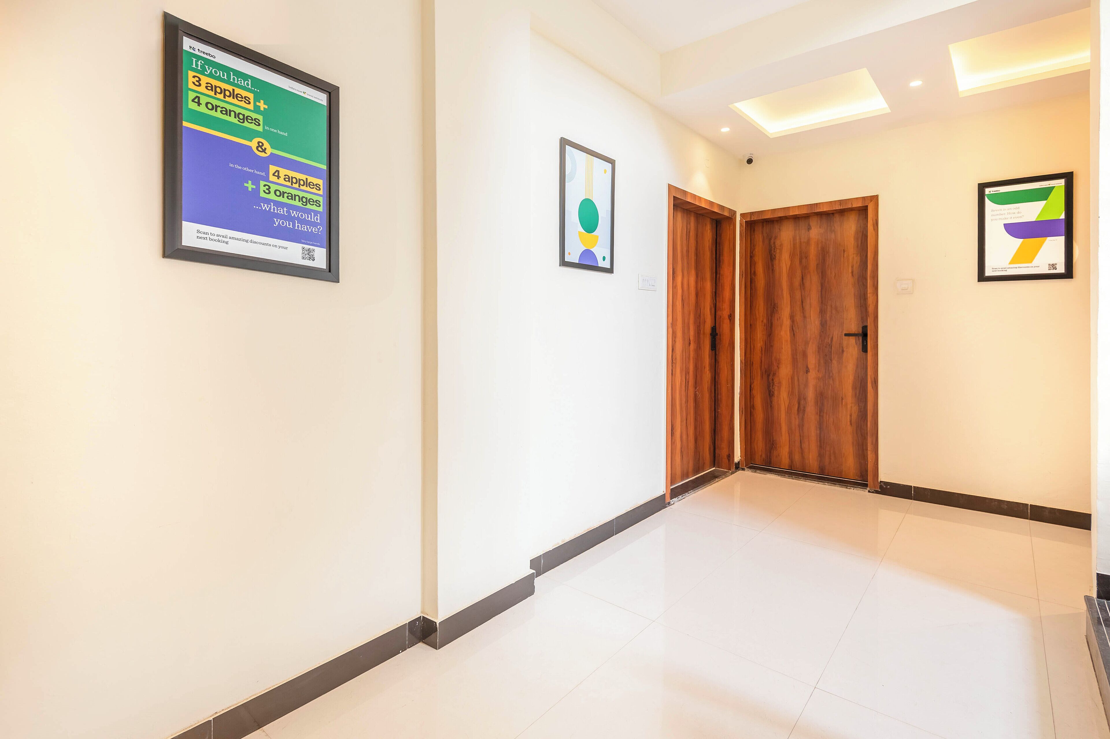 A hallway with white walls, a wooden door, and framed artwork.