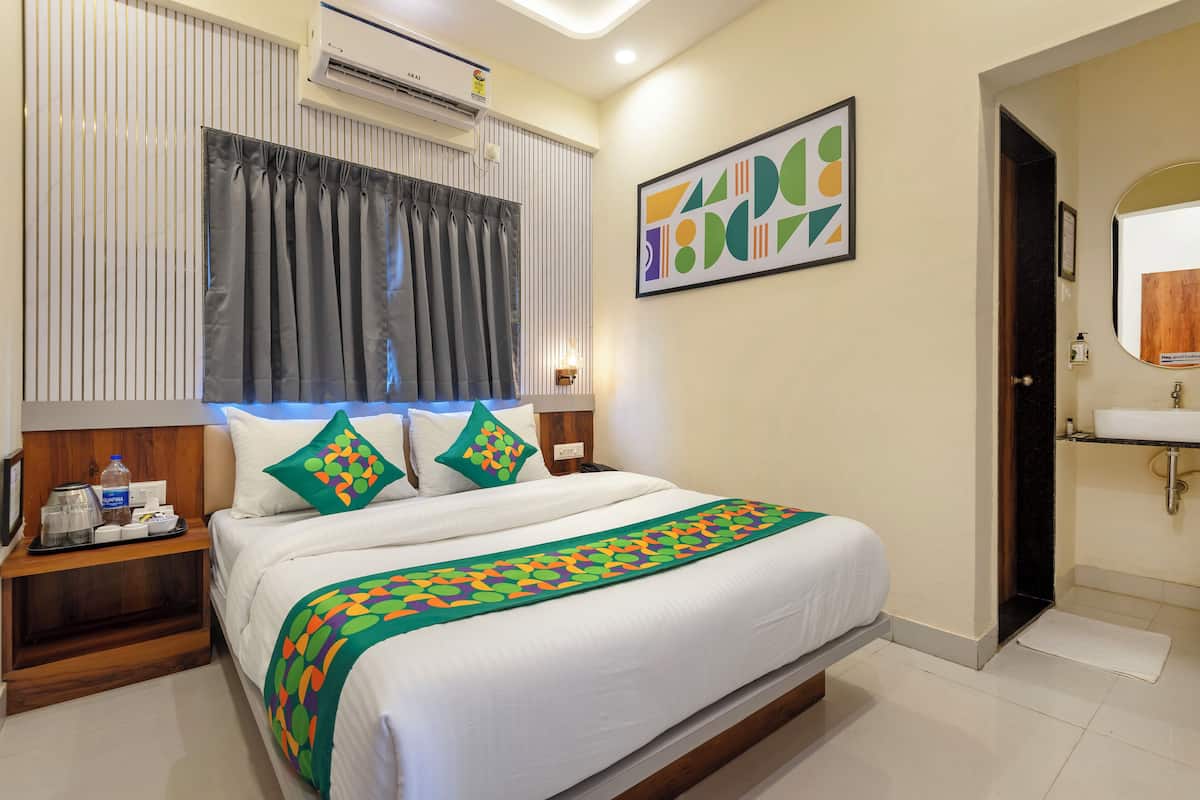 Une chambre d’hôtel avec un lit, une table de chevet, une salle de bain avec un lavabo et une fenêtre avec des rideaux.