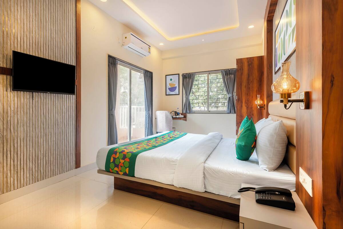 Une chambre d’hôtel moderne équipée d’un lit, d’un téléviseur à écran plat, d’un climatiseur et d’un téléphone posé sur une table de chevet.