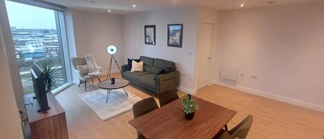 Un vaste espace de vie comprenant une grande fenêtre, un canapé, une table basse et une table à manger avec des chaises.