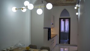 Comedor con mesa de madera preparada para cuatro, cocina al fondo y un pasillo que conduce a otra habitación.