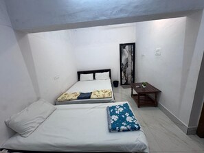 A small, single-room accommodation with two beds, a small table, and a painting on the wall. - Silver Sand Beach Homestay (Bhatkal)