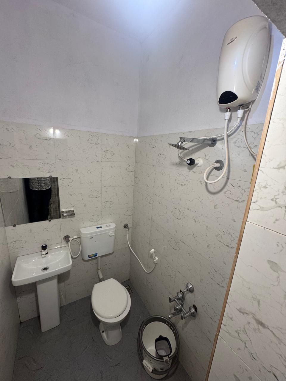 Un baño con inodoro, lavamanos y cabezal de ducha manual instalado en la pared.